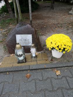 Znicze i kwiaty przy tablicy upamiętniającej patrona szkoły.